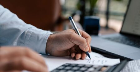 Free A person calculating finances with a calculator and pen on a desk indoors. Stock Photo