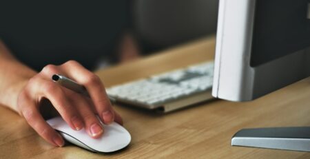 Free A hand using a wireless mouse at a modern desk setup with a computer and keyboard. Stock Photo