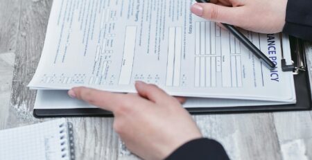 Free Close-up of hands analyzing insurance policy paperwork with pen on table. Stock Photo